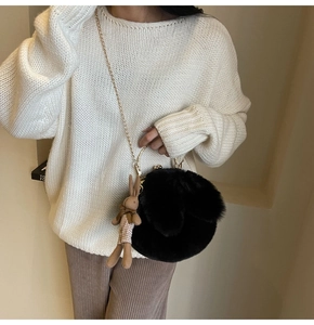 Detail of round black faux fur bag with golden chain and cute bunny plush charm