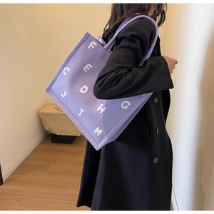 Detail of a large purple canvas tote bag with white letters worn over a black winter coat