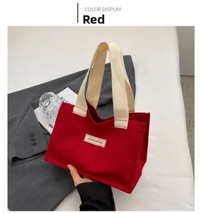 Détail d'un sac cabas en toile rouge avec anses larges blanc cassé et étiquette