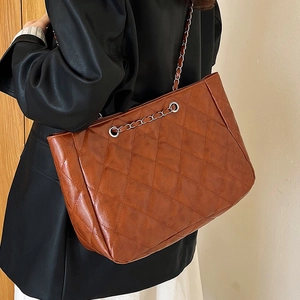 Brown quilted leather tote bag with silver chain straps shown on a model in a casual setting