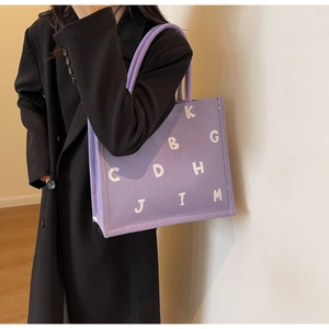 Detail of purple canvas tote bag featuring white letter prints and thick rope handles