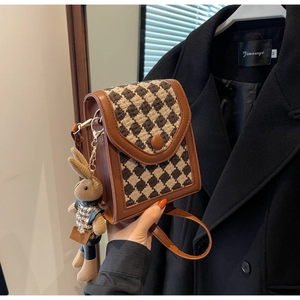 Close-up of brown vintage checkered flap bag with a cute knitted bunny doll charm