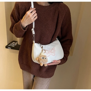 Détail du sac demi-lune en cuir litchi blanc avec broderie papillon et breloque en peluche