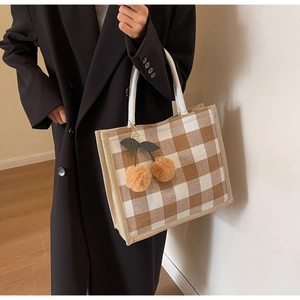 Detail of waffle plaid tote bag with cherry pompom charm and woven rope handle