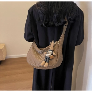 Détail du sac hobo matelassé marron foncé avec breloque lapin porté par un mannequin