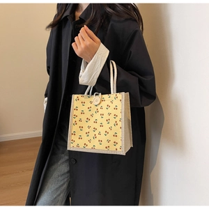 Detail showing cherry print canvas bag with white cotton rope handles and button closure