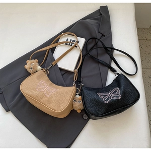 Détail du sac bandoulière en cuir grainé avec broderie papillon rose et breloque ours doux