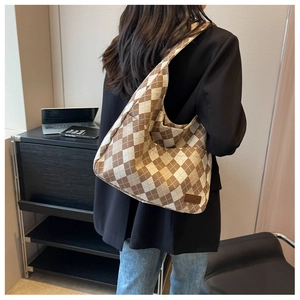 Detail of a large brown and white checkered tote bag with a fashion label on a model