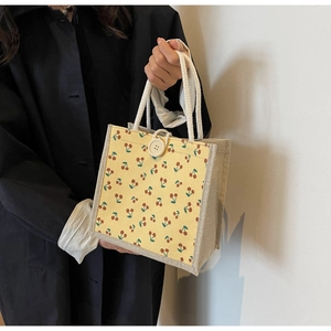 Detail of yellow corduroy tote bag with cherry print, linen texture, and rope handles