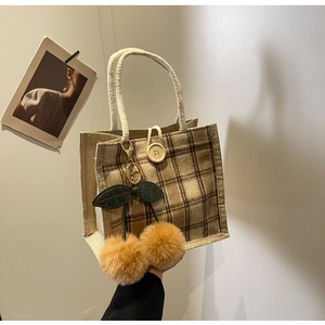 Detail of checkered jute lunch bag featuring white rope handle and cherry pompom charm
