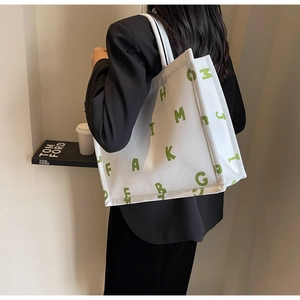 Detail of white canvas tote bag with green letter print and wide shoulder strap