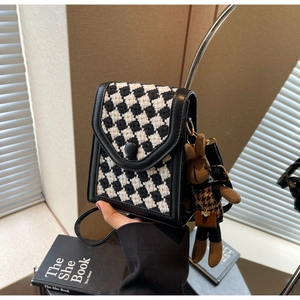 Detail of houndstooth crossbody phone bag with a cute brown bear charm accessory