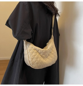 Detail of beige quilted half-moon crossbody bag shown on model with adjustable strap