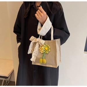 Detail of jute handbag featuring white lace bow and hand-woven flower pendant charm