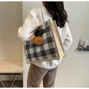 Detail view of large linen tote bag with black and white plaid pattern and fuzzy pompom