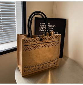 Detail of jute tote bag with black geometric patterns and woven handles on a metal table