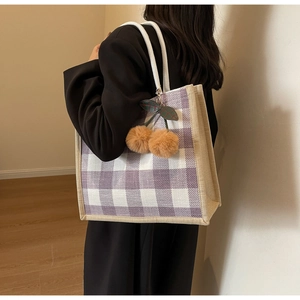 Detail of purple waffle knit tote bag with plush cherry charm on a model's shoulder