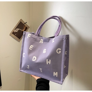Detail of purple canvas tote bag featuring white letter prints and sturdy handles