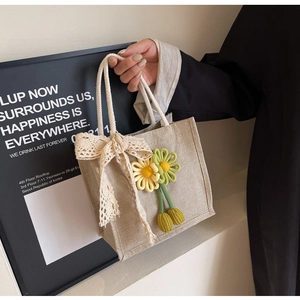 Close-up of linen tote bag with lace bow and handmade knitted floral pendants