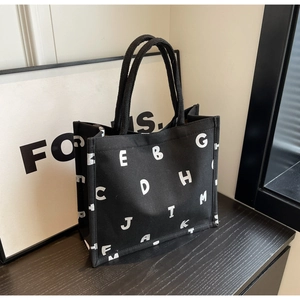 Detail of black canvas tote bag with white letter print and reinforced handles
