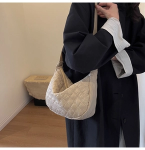 Detail of light beige quilted crossbody bag with soft padded texture and crescent shape