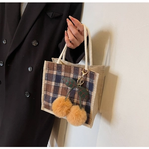Detail of woven plaid tote bag featuring plush cherry charms and white rope handle