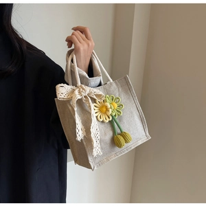 Close-up of linen lunch bag with lace bow and knit floral charms on braided handles
