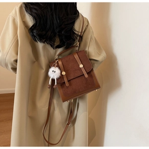 Detail of vintage brown shoulder bag with plush monster charm on a beige trench coat