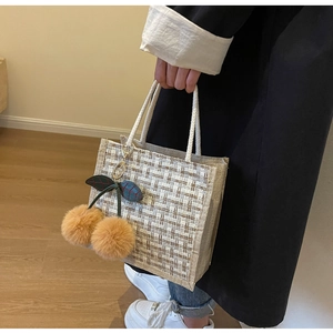 Detail view of woven tote bag with white rope handle and fuzzy cherry charm pendant