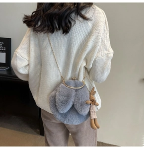 Detail of grey plush bunny crossbody bag with gold chain and rabbit charm on white sweater
