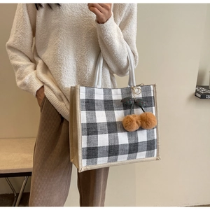 Checkered linen tote bag with cherry pom-pom charm shown in a fashion lifestyle setting