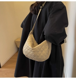 Detail of beige quilted crescent bag featuring adjustable strap on black coat