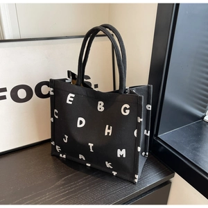 Detail of black canvas tote bag with white letter print on a minimalist textured surface