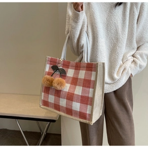 Detail of red checkered linen tote bag with plush cherry charm and reinforced piping