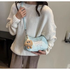 Détail du sac bandoulière bleu clair avec broderie papillon rose et breloque peluche