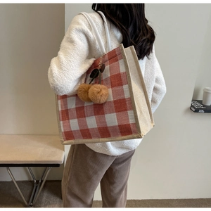 Close-up of red checkered linen tote bag featuring brown pompom charms and woven texture
