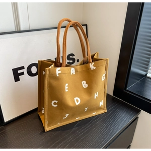 Close-up of mustard yellow canvas tote bag with white letter print and woven handles