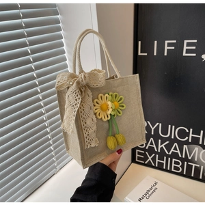 Close-up of beige jute tote bag featuring handmade 3D floral accents and a lace bow