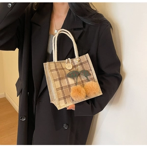 Detail of brown plaid lunch bag with cherry pom-pom charm and woven rope handles