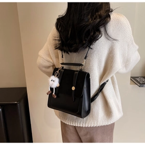 Close-up of black structured backpack with plush pendant and metal buckle detail