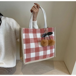 Detail of red and white checkered linen tote bag with plush cherry charm accessory