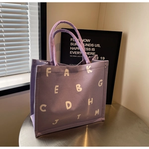 Detail of purple canvas tote bag with white letter print on a stylish metal table