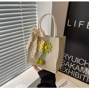 Detail of beige linen tote bag with yellow knit sunflower and delicate lace bow accent