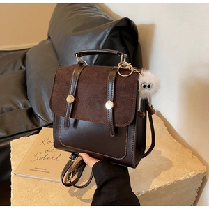 Detail of dark brown vintage backpack with gold buckles and plush charm on stone pedestal