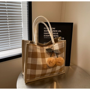 Detail of checkered linen tote bag with plush cherry pendant on a metal table