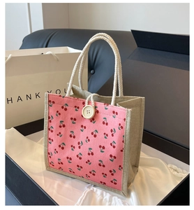 Close-up of pink corduroy handbag featuring red cherry patterns and braided rope handles