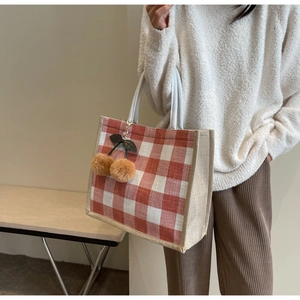 Detail of red and white plaid waffle tote bag with a cute plush cherry charm hanging on side