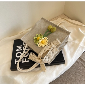 Detail of linen lunch tote bag with woven flowers, lace bow and white rope handle