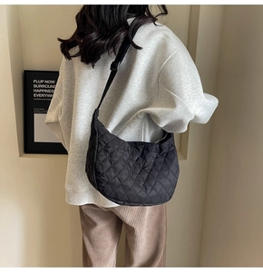 Rear view of black quilted crescent crossbody bag worn by model over a grey sweatshirt