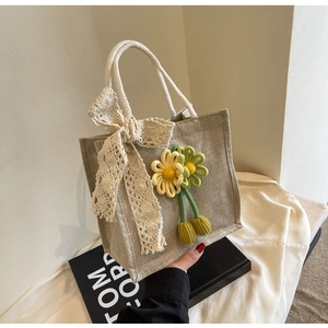 Detail of jute bento bag with lace bow and crochet floral charms on a fabric background